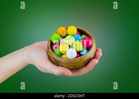 Bright candy chewing gum in a wooden bowl dish lies on the palm of hand on a green background macro