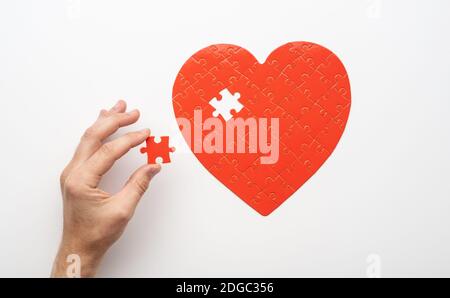 Top view of hand holding last piece near unfinished puzzle in form of heart on white background Stock Photo