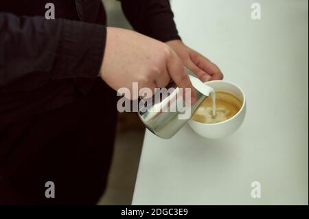 Hands of baristas pouring milk into a cup of coffee Stock Photo