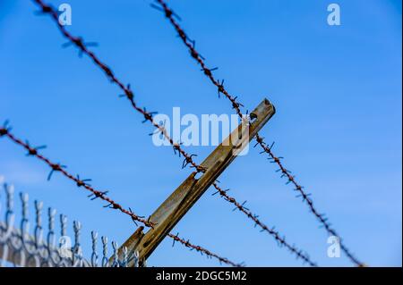 Focus on part of rusted metal barb wire fence against blue sky. Stock Photo