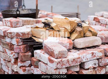 Folded brazier of bricks in lime, heat resistant with a stock of birch firewood and a pot Stock Photo