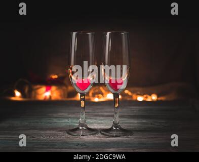 Romantic background with champagne glasses and hearts on the background of a burning garland in the dark. Stock Photo