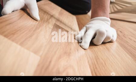 Installing laminated floor, detail on man hands in white gloves fitting wooden tiles Stock Photo