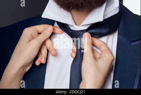 Womens hands tie around the neck of men classic suit model beard Stock Photo