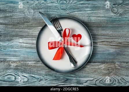 February 14, romantic background with a plate, Cutlery with a bow and a heart on a wooden background. Stock Photo