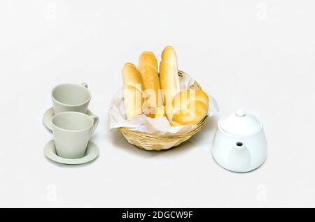 Breakfast with a full bread basket cups and teapots on a white background Stock Photo