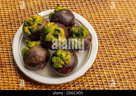 A pile of mangosteen lies on a plate, dark lilac fruits on a wooden background Stock Photo