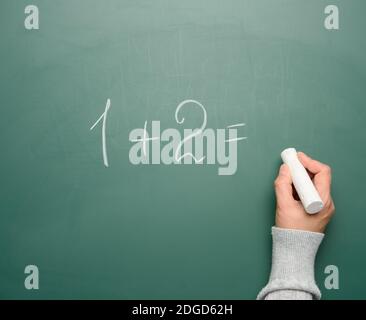 math example written in white chalk on a green chalk board and a woman's hand with white chalk, one plus two Stock Photo