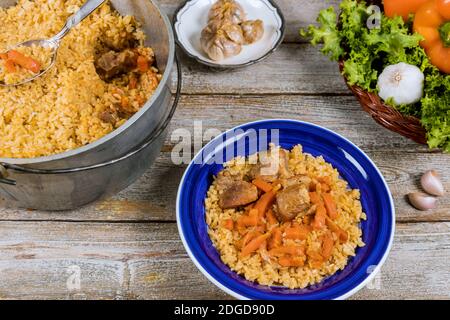 Traditional uzbek meal called pilaf rice with meat, carrot and onion in plate on vintage wooden background Stock Photo