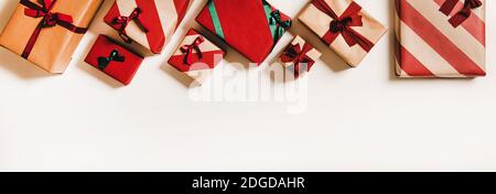 Flat-lay of festive craft gift boxes in wrapping paper decorated with colorful baubles, ribbons and bows over plain white background, top view, copy space. . Christmas boxing day concept Stock Photo