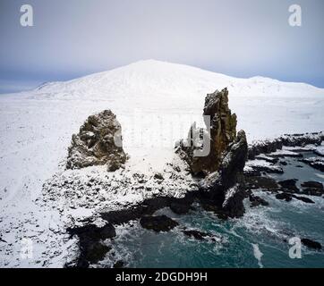 Scenic drone view of rough rocks on shore near sea covered with snow in Iceland Stock Photo