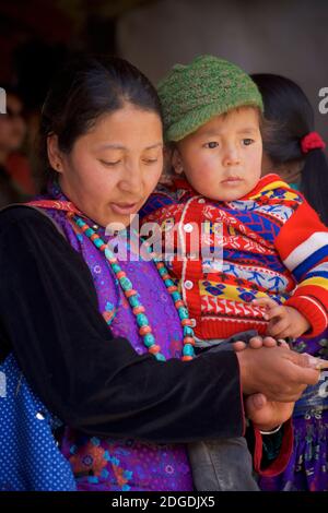 Ladakhi mother in festive dress carrying young child. Karsha Gustor festival, Karsha monastery, near Padum Zanskar Valley, Ladakh, Jammu and Kashmir, northern India Stock Photo