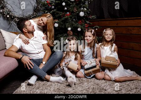 Happy cute family with three children exchanging gifts under the Christmas tree on the carpet. Family and holiday concept. Stock Photo