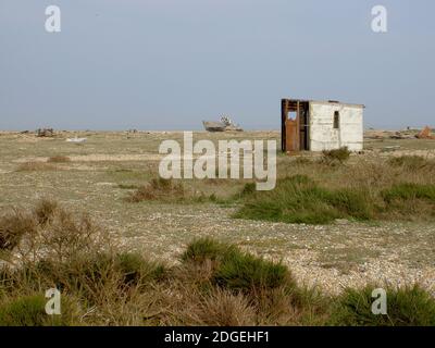 Dungeness, U.K. Abandoned fishermen's hut and a derelict boat's hull. In the foreground beach plants and grasses growing on the shingle. Stock Photo