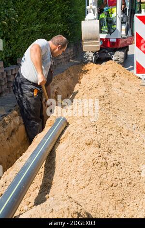 Workers installing underground optical fiber cables in road excavation street construction site. Stock Photo