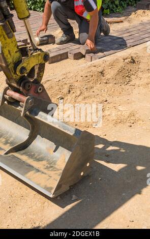 The worker lays paving stones in layers, using hammer to solidify the stones on the ground for repairing the pedestrain sidewalk next to the street. Stock Photo
