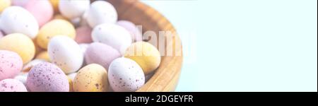 Easter banner. Easter eggs in wooden bowl on blue background. Selective focus with copy space. Close-up. White yellow pink eggs for Easter treat. Stock Photo