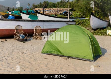 Green tent and old wicker chairs next to fishing boats on the beach in Goa in India Stock Photo