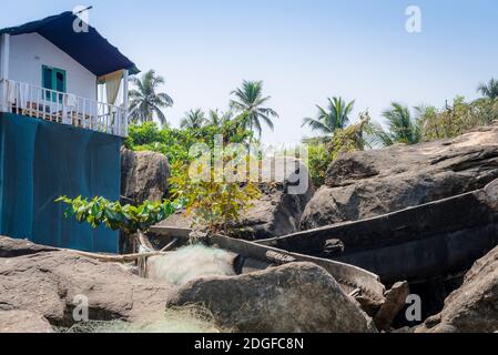 PALOLEM, GOA, INDIA - MARCH 19, 2019: View of old broken wooden boats and fishing nets on a rocky slope next to a village house in Palolem, Goa, India Stock Photo