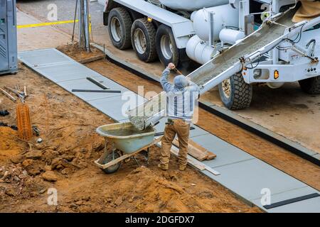 Construction worker pour cement for sidewalk in concrete works with mixer truck with wheelbarrow Stock Photo