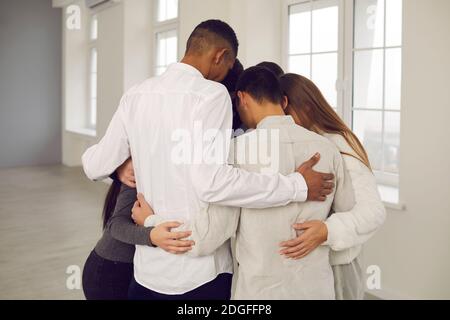 Team of young colleagues or students standing in circle and embracing each other Stock Photo
