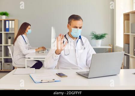 Middle aged man doctor in protective medical mask communicating online with patient Stock Photo