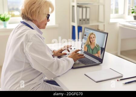 Side view of a senior female family doctor using laptop for online consultation with her patient. Stock Photo