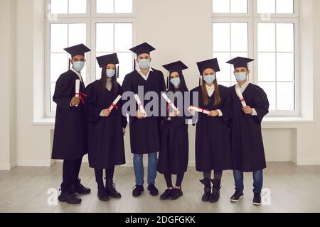Portrait of successful students with diplomas in their hands and with medical masks on their faces. Stock Photo
