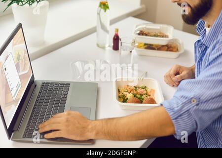 Man signing up for food delivery website using laptop while having lunch break in the office Stock Photo
