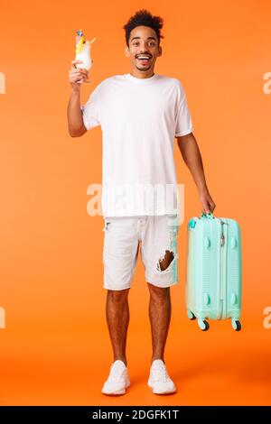 Full-length vertical shot happy african-american guy on vacation, holding luggage as travel, saying hi friends in hotel, drinkin Stock Photo
