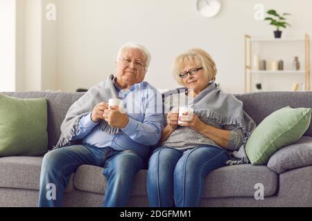Portrait of a senior couple wrapped in a plaid sitting on the couch and drinking hot tea. Stock Photo