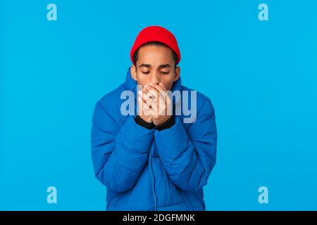 Man feeling cold, trying warm himself as blowing hot breathing at palms, trembling standing in snowy low temprature weather in b Stock Photo