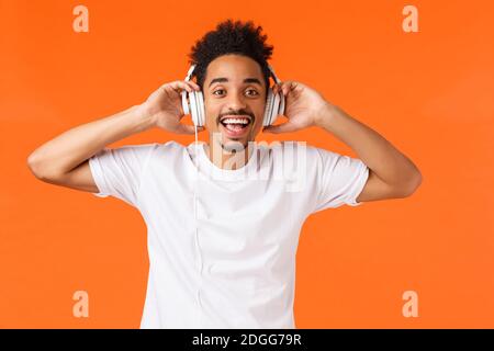 Happy and cheerful handsome african-american man, listen music in headphones, enjoying new single of artist, look camera questio Stock Photo