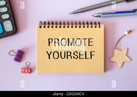 PROMOTE YOURSELF is written on a notepad on an office desk with office accessories. Stock Photo