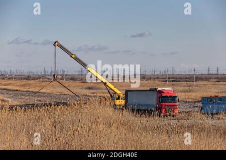 Loading of large-diameter steel pipes in the steppe using a truck crane Stock Photo
