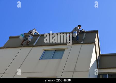 Bangkok, Thailand- December 9, 2020: Two workers are repairing cracked wall outside a high-rise building by using sealant silicone and painting Stock Photo