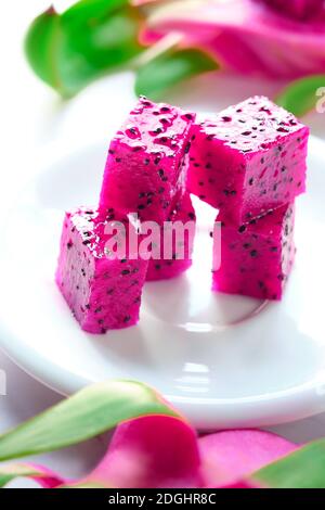 Pink dragon fruit, pitaya or pitahaya cut in cubes on white plate on the table. Trendy superfood.