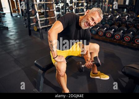 Smiling gray-haired bodybuilder doing the concentration curl Stock Photo