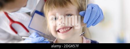 Dentist doctor examines teeth of little smiling girl in clinic Stock Photo