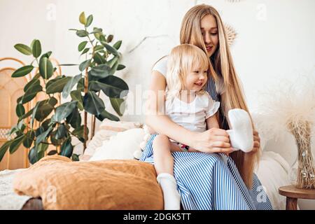 Young mom or babysitter puts on socks to a three year old child Stock Photo