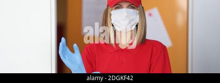 Woman in red uniform and medical protective mask on her face puts rubber glove on her hand. Stock Photo
