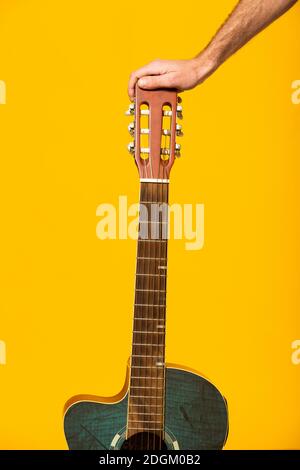 Human hand holding a blue acoustic guitar against a yellow background Stock Photo
