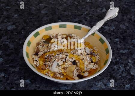 Green and Yellow Breakfast Bowl with a helping of muesli, yoghurt and honey.Silver Dessert spoon. Delicious.  On a blue gray granite background. Stock Photo