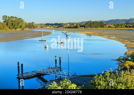 A channel in a sandy harbor at low tide, with a floating pier and a group of small boats on the water. Photographed in the Bay of Plenty, New Zealand Stock Photo