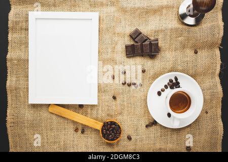 A cup full of espresso with chocolate and coffee beans and candles and a picture frame. Flat lay overhead shot. Stock Photo