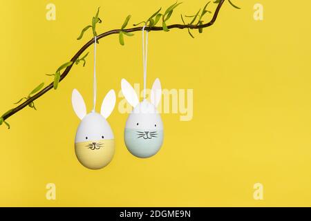 Two easter egg ornaments with happy bunny faces hanging on a branch on a yellow background Stock Photo