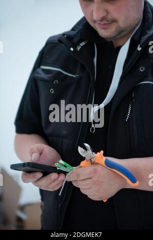 Electrical engineer with wire and pliers in his hand using mobile phone Stock Photo