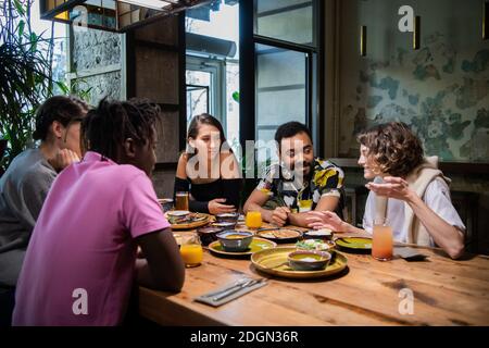 Young multi-ethnic friends celebrating something in a cafe. Stock Photo