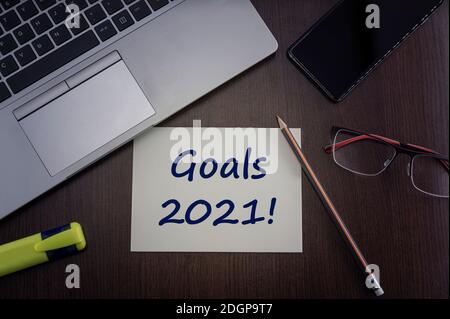 Goals 2021 card. Top view of office table desktop background with laptop, phone, glasses and pencil with card with inscription we can do it.  Business Stock Photo