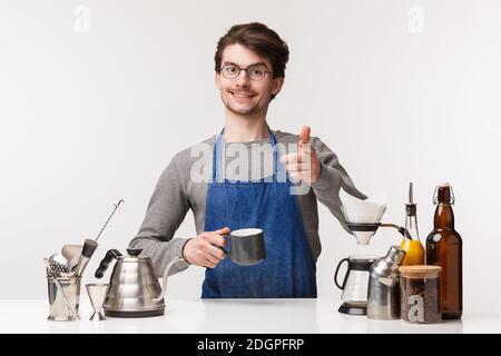 Barista, cafe worker and bartender concept. Friendly pleasant caucasian guy in apron make finger pistol gesture and smiling at c Stock Photo